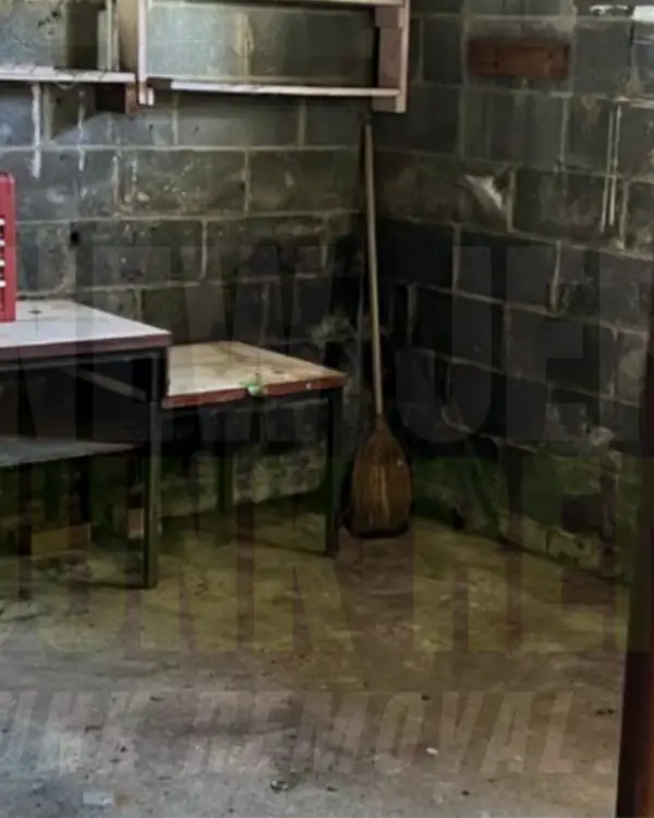 After: the same basement corner cleared, with a work table and a broom left in place