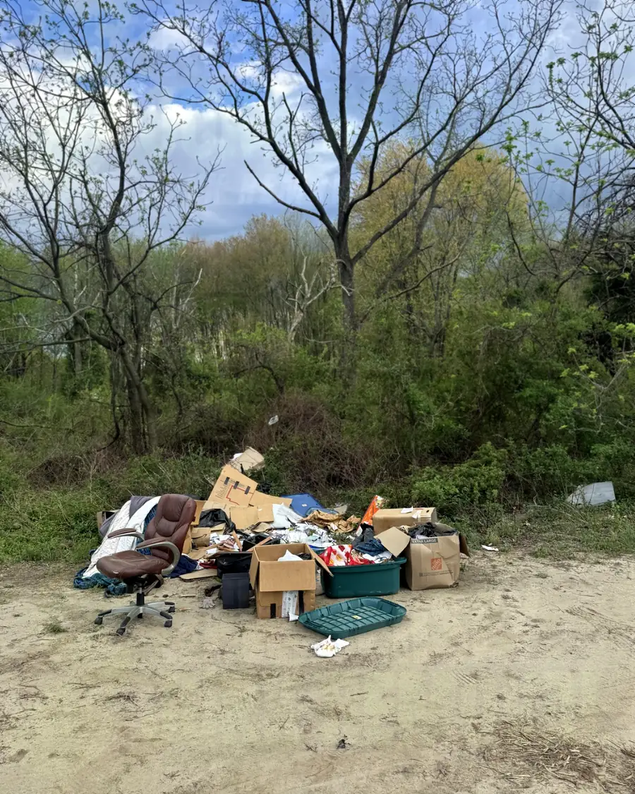 Before: a heap of dumped furniture, an office chair, boxes and debris on a sandy lot
