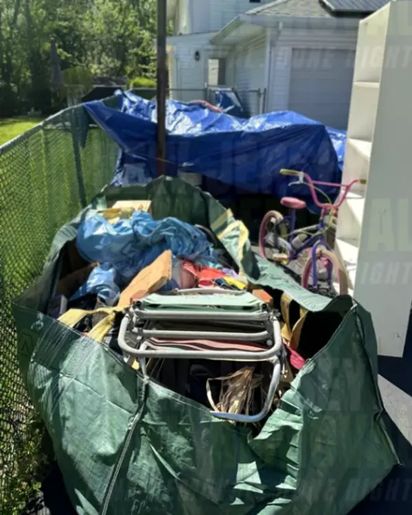Before: a full dumpster bag of household junk on a driveway, with a white bookshelf and a kids' bike beside it