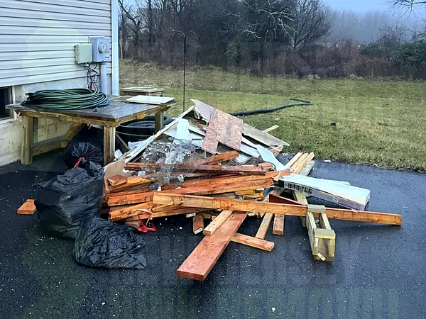 Scrap lumber, plywood and bags of debris piled on a driveway beside a house