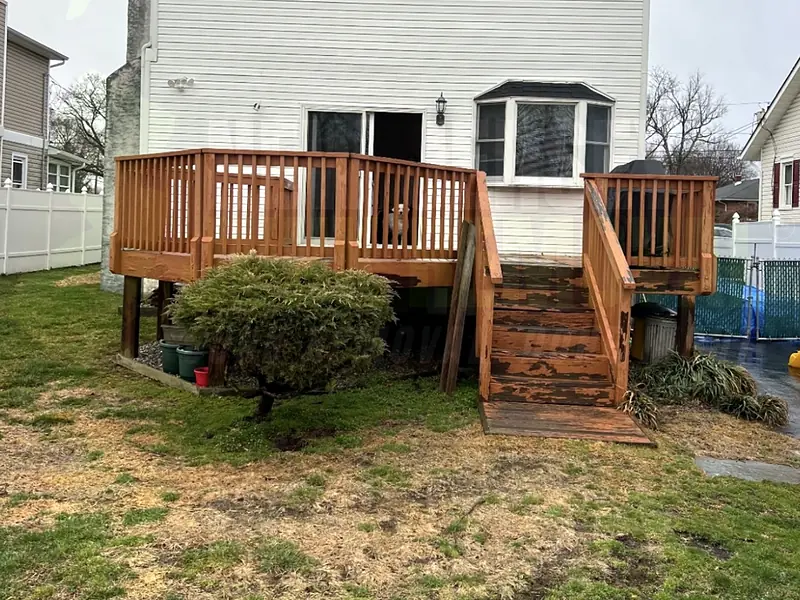The back of a house with a raised wooden deck and stairs before removal